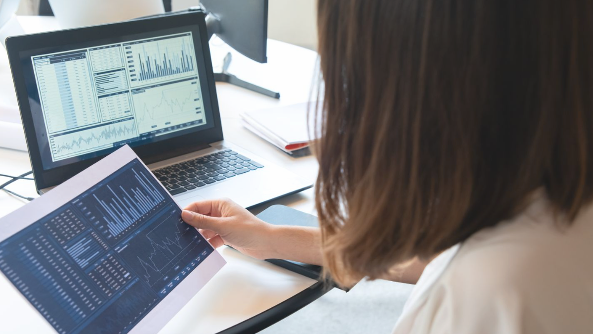 Profissional analisando gráficos impressos ao lado do notebook com dados na tela