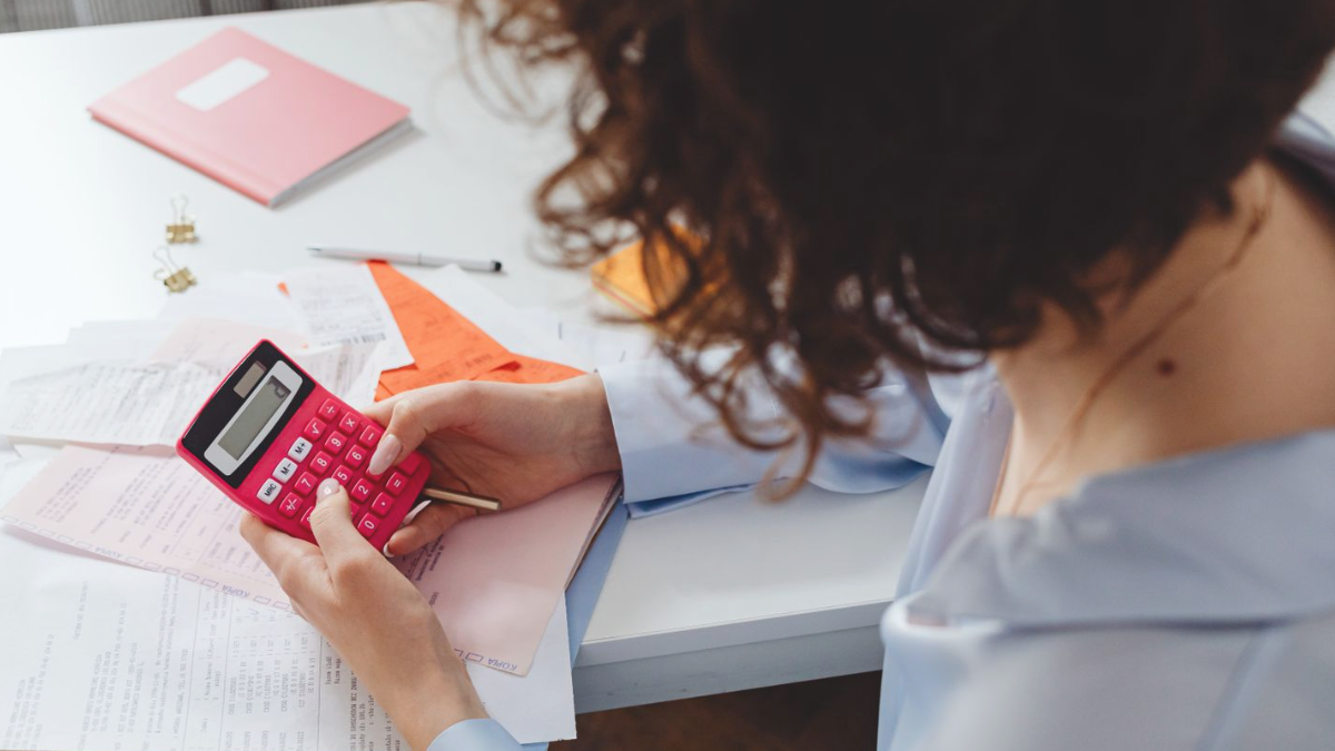 Mulher usando calculadora para revisar contas e recibos sobre a mesa