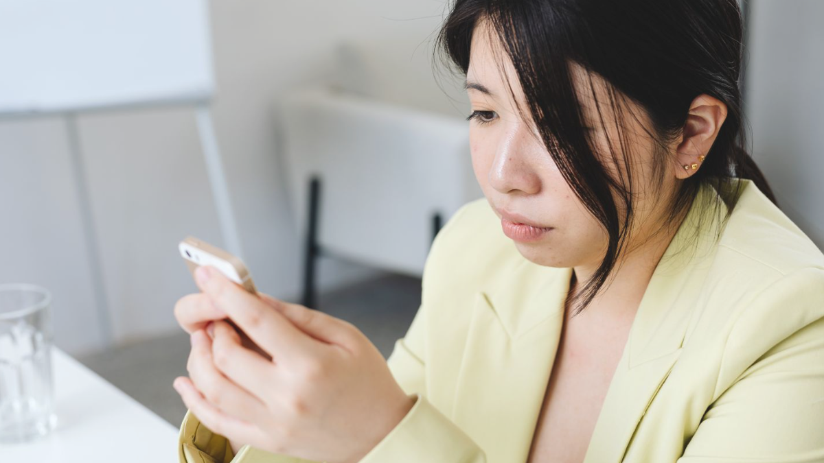 Mulher séria olhando para o celular enquanto responde uma mensagem