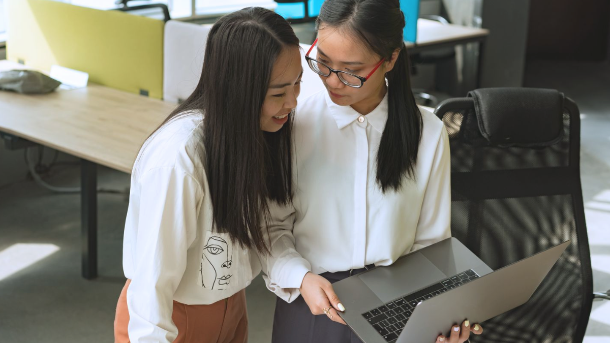 Duas colegas revisando informações juntas no notebook em um escritório
