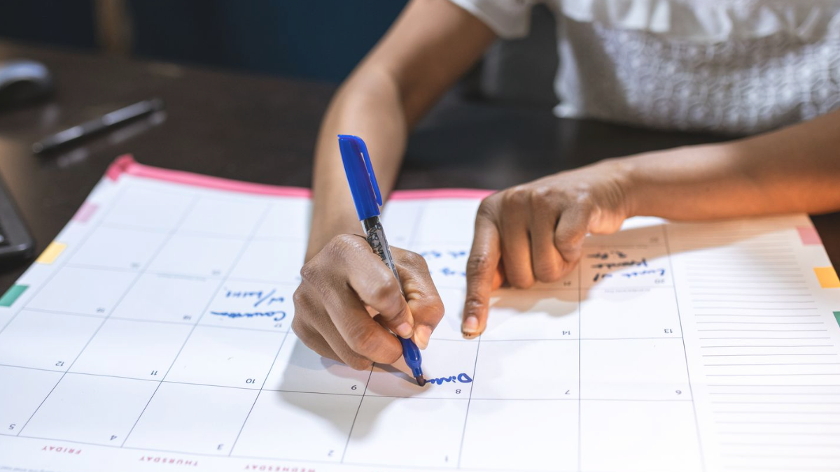 Mãos preenchendo compromissos em uma agenda de mesa grande