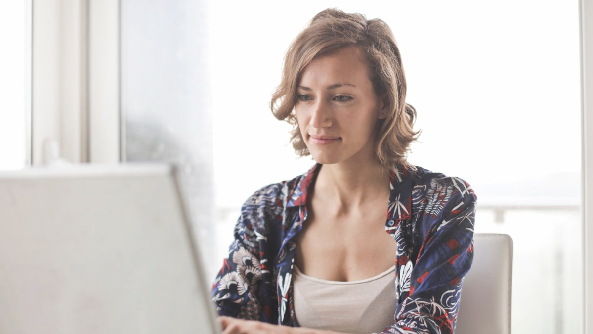 Mulher de camisa estampada sentada diante de um notebook aberto junto a uma janela clara, conferindo se a empresa aparece no ChatGPT.