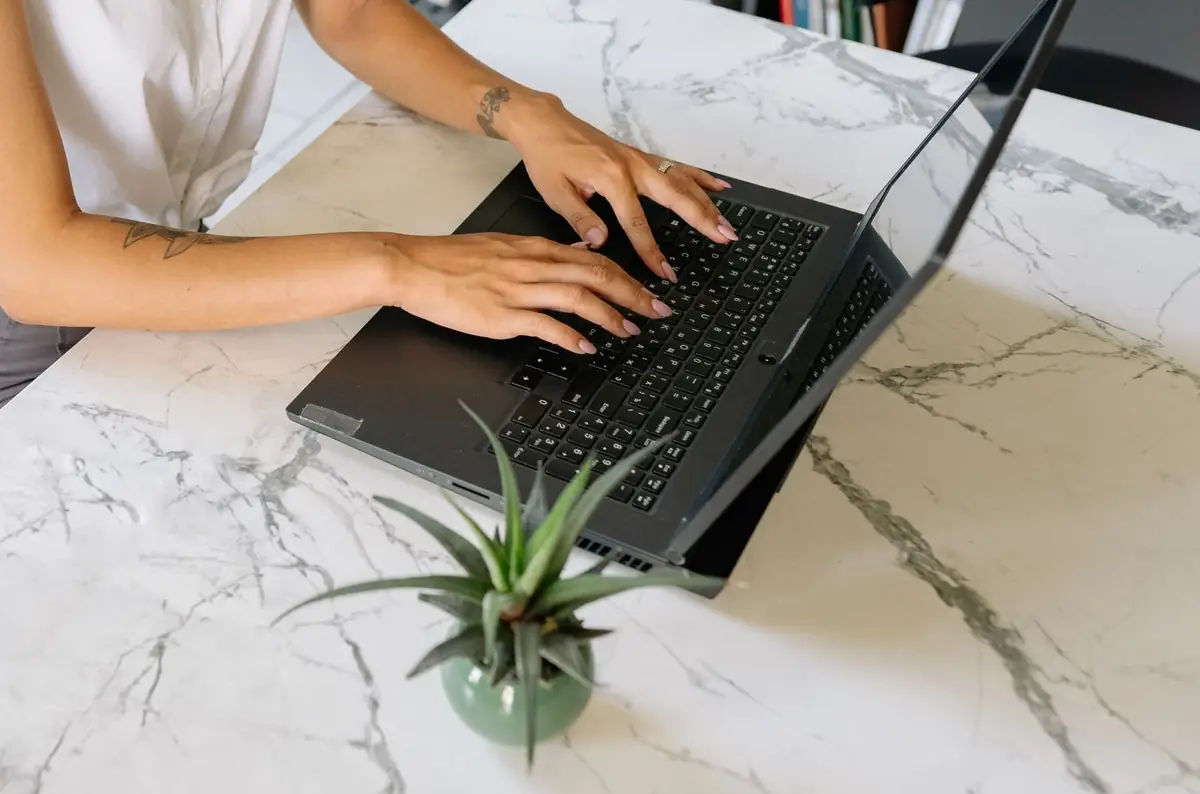 Mãos digitando em um notebook sobre mesa de mármore