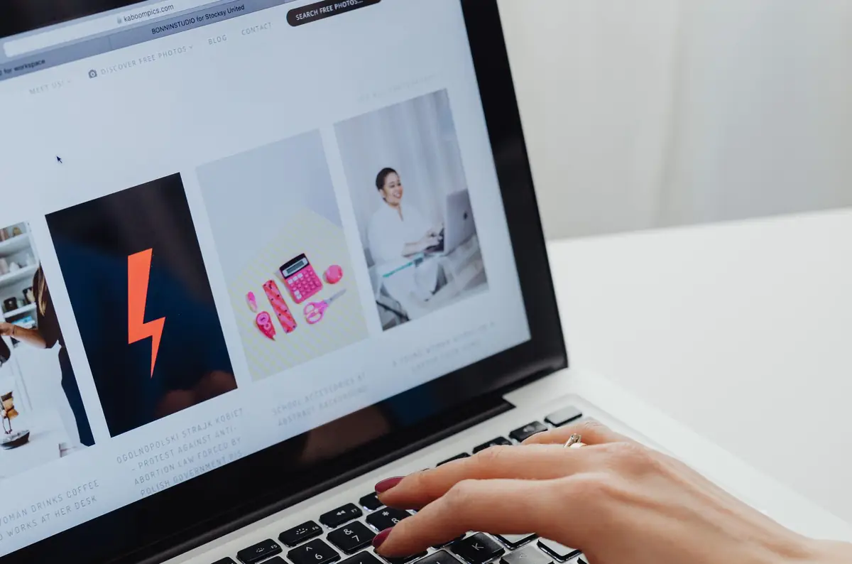 Mão feminina no teclado de um notebook com um site aberto na tela