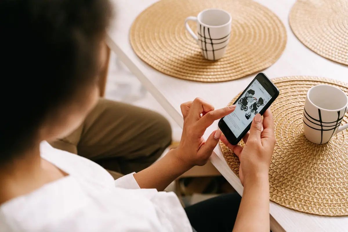 Mulher pesquisando no celular sentada à mesa, antes de marcar uma consulta