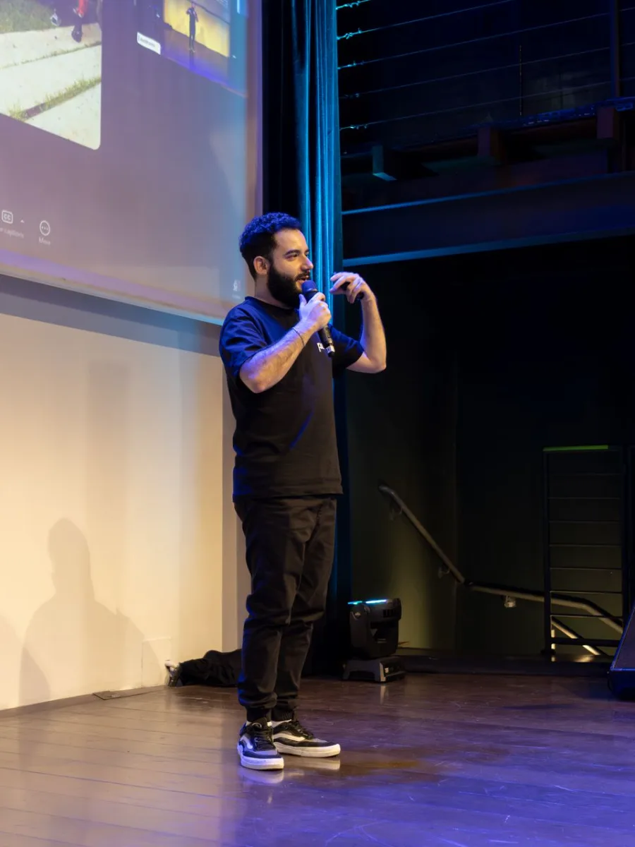 Palestrante no palco com microfone, com a tela de projeção ao fundo