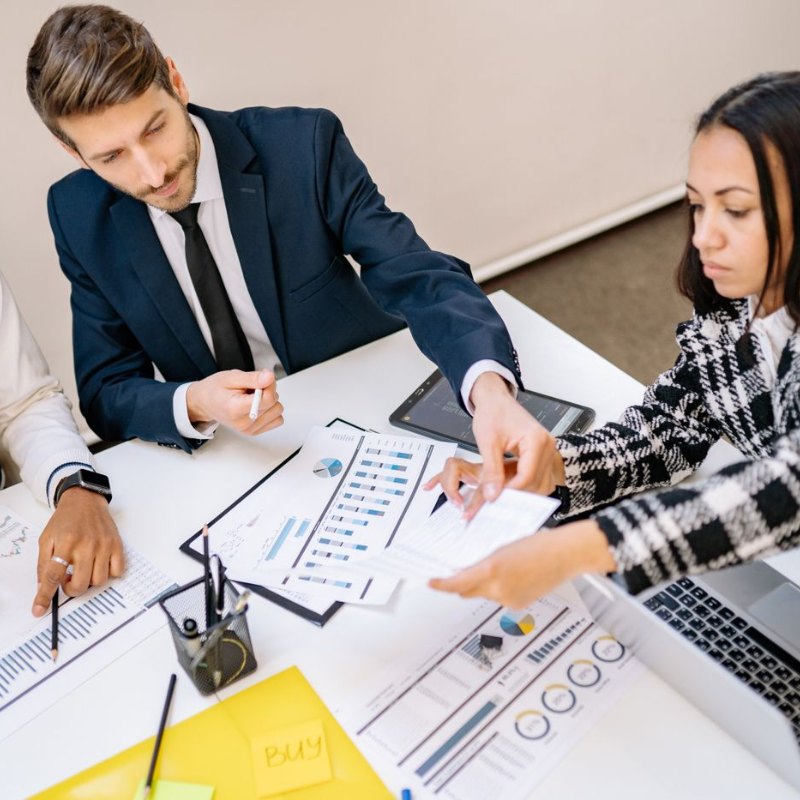 Duas pessoas em reunião de trabalho analisando anotações e gráficos sobre a mesa.