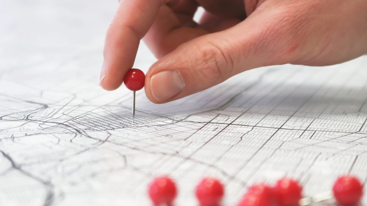 Mão fixando alfinete num mapa, ilustrando área de atendimento de quem quer ter perfil da empresa no Google